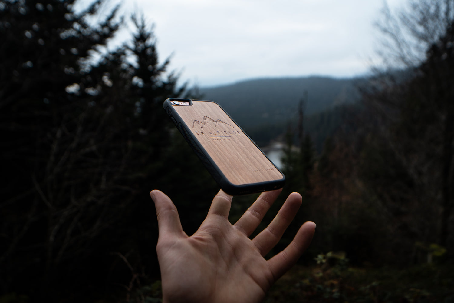 La main d'un homme dans la nature avec une coque de téléphone en bois pour iPhone SE, modèle En Altitude.