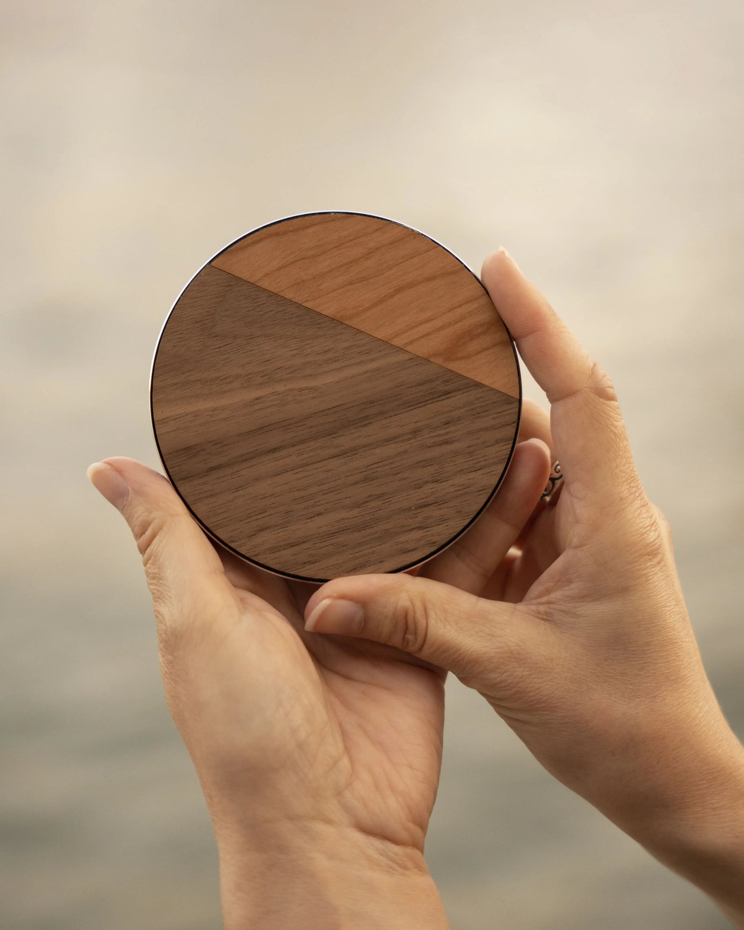 Personne qui tient un chargeur à induction en bois pour téléphones dotés de la technologie Qi. Fabrication artisanale et française par l'assemblage de deux essences de bois véritable, modèle Le Duo.