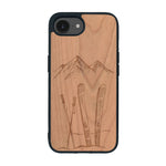 Coque de protection en bois véritable fabriquée en France pour iPhone 16e sur le thème de la montagne, du ski et de la neige avec un motif représentant une paire de ski plantée dans la neige avec en fond des montagnes enneigées