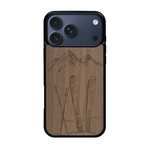Coque de protection en bois véritable fabriquée en France pour iPhone 17 Pro Max sur le thème de la montagne, du ski et de la neige avec un motif représentant une paire de ski plantée dans la neige avec en fond des montagnes enneigées