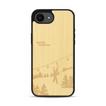 Coque de protection en bois véritable fabriquée en France pour iPhone 17e sur le thème de la montagne, du ski et de la neige avec un motif représentant une paire de ski plantée dans la neige avec en fond des montagnes enneigées