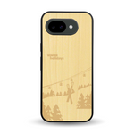 Coque de protection en bois véritable fabriquée en France pour Google Pixel 10A sur le thème de la montagne, du ski et de la neige avec un motif représentant une paire de ski plantée dans la neige avec en fond des montagnes enneigées