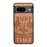 Coque de protection en bois véritable fabriquée en France pour Google Pixel 7A sur le thème chill avec un motif représentant une silouhette tenant une planche de surf sur une plage entouré de palmiers et les mots "Surf Time Long Beach Miami"