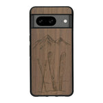 Coque de protection en bois véritable fabriquée en France pour Google Pixel 7A sur le thème de la montagne, du ski et de la neige avec un motif représentant une paire de ski plantée dans la neige avec en fond des montagnes enneigées