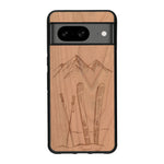 Coque de protection en bois véritable fabriquée en France pour Google Pixel 8 sur le thème de la montagne, du ski et de la neige avec un motif représentant une paire de ski plantée dans la neige avec en fond des montagnes enneigées