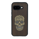 Coque de protection en bois véritable fabriquée en France pour Google Pixel 9A alliant du chêne fumé avec du métal argenté et doré représentant une tête de mort mexicaine sur le thème Dia de los Muertos