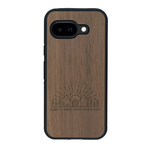 Coque de protection en bois véritable fabriquée en France pour Google Pixel 9A sur le thème chill et nature avec un motif représentant un levé de soleil sur un paysage de montagne avec des sapins et un chalet et la phrase "Good friends, good adventure"