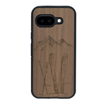 Coque de protection en bois véritable fabriquée en France pour Google Pixel 9A sur le thème de la montagne, du ski et de la neige avec un motif représentant une paire de ski plantée dans la neige avec en fond des montagnes enneigées