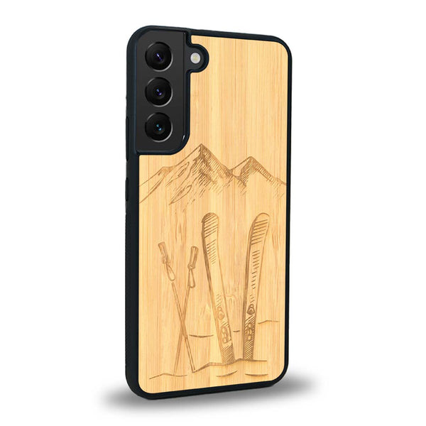 Coque de protection en bois véritable fabriquée en France pour Samsung S24 sur le thème de la montagne, du ski et de la neige avec un motif représentant une paire de ski plantée dans la neige avec en fond des montagnes enneigées