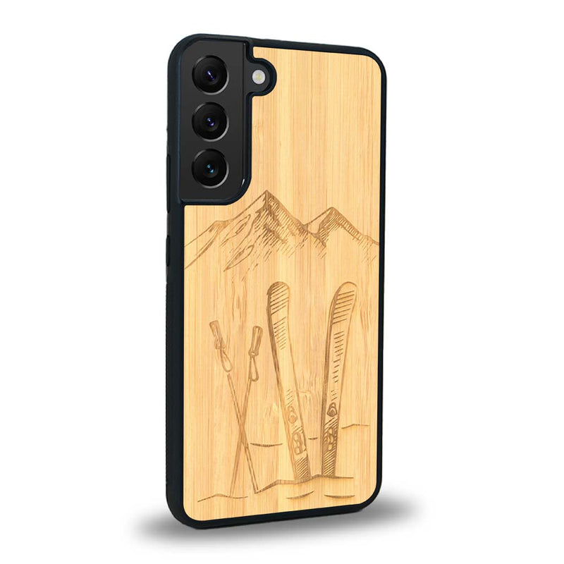 Coque de protection en bois véritable fabriquée en France pour Samsung S24+ sur le thème de la montagne, du ski et de la neige avec un motif représentant une paire de ski plantée dans la neige avec en fond des montagnes enneigées