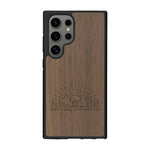 Coque de protection en bois véritable fabriquée en France pour Samsung S25 Ultra sur le thème chill et nature avec un motif représentant un levé de soleil sur un paysage de montagne avec des sapins et un chalet et la phrase "Good friends, good adventure"