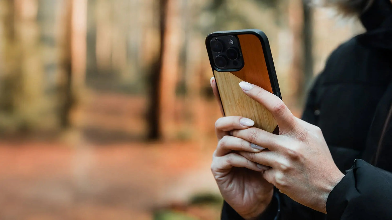 Une femme tenant un téléphone avec une coque en bois modèle Le Trio pour iPhone 13 Pro.