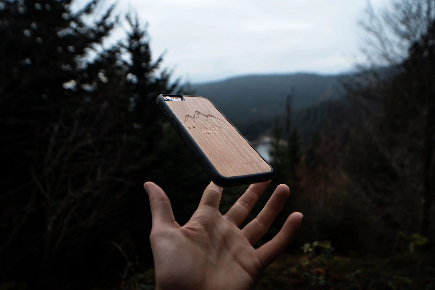 La main d'un homme dans la nature avec une coque de téléphone en bois pour iPhone SE, modèle En Altitude.