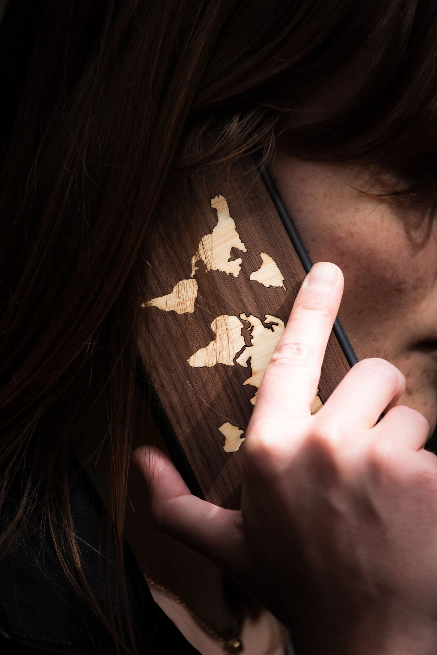 Femme au téléphone avec une coque en bois modèle Le Mappemonde, fabriquée en France et artisanale.