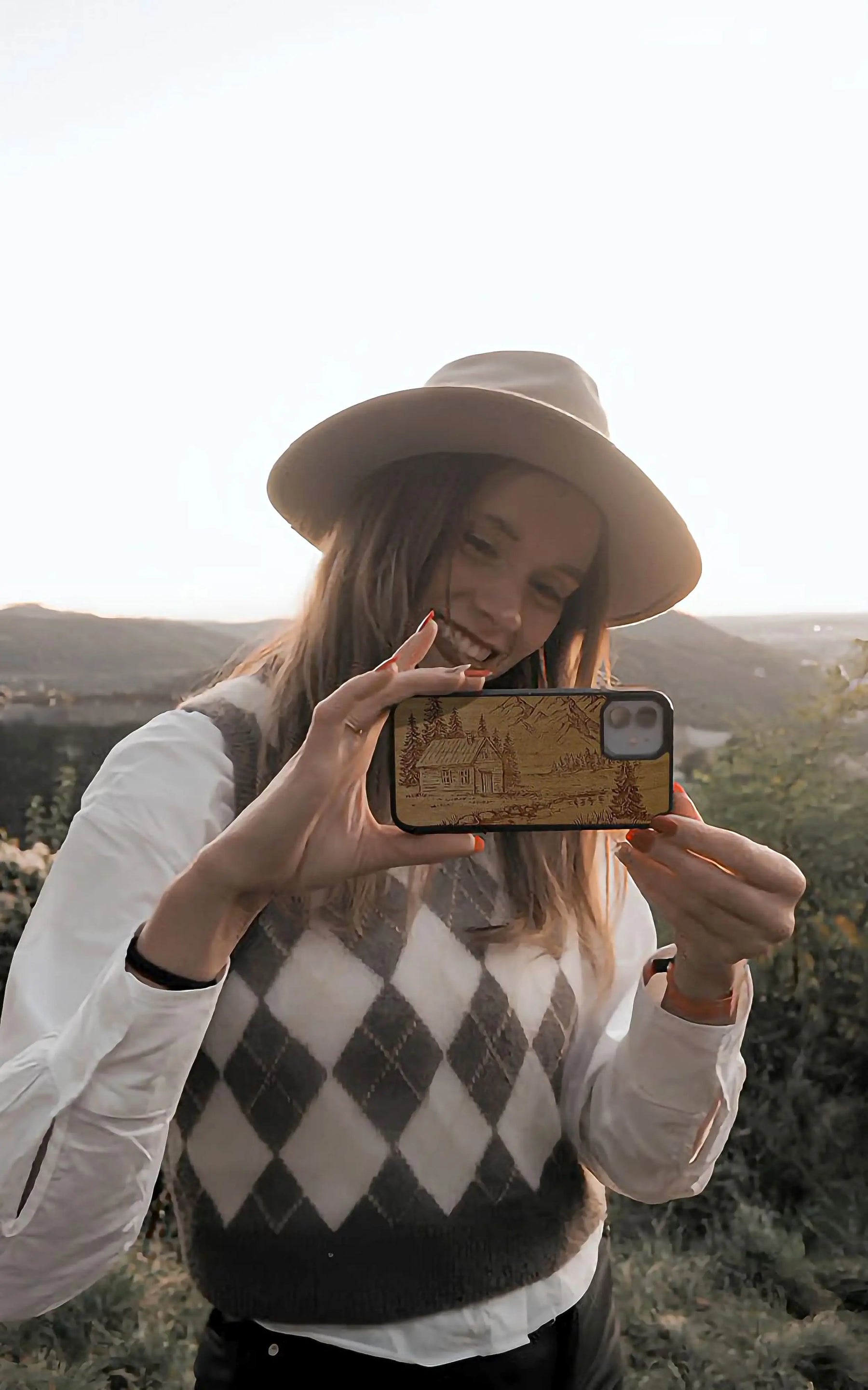 Femme dans la nature qui tient son téléphone avec une coque en bois personnalisée avec une montagne pour iPhone 11.