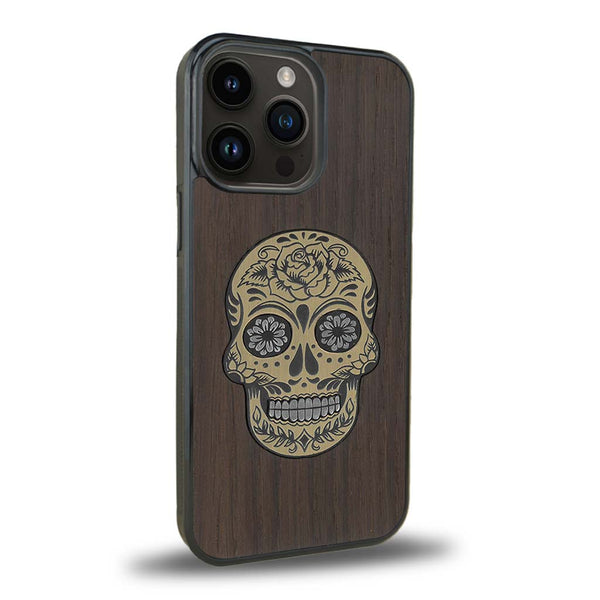 Coque de protection en bois véritable fabriquée en France pour iPhone 15 Pro alliant du chêne fumé avec du métal argenté et doré représentant une tête de mort mexicaine sur le thème Dia de los Muertos