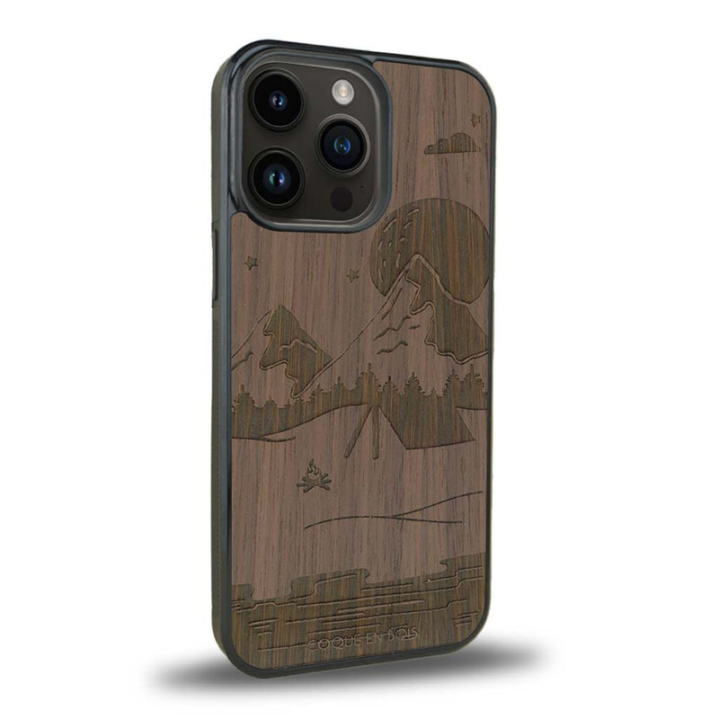 Coque de protection en bois véritable fabriquée en France pour iPhone 15 Pro sur le thème du camping en pleine nature représentant une tente avec un feu de camp entouré de montagnes