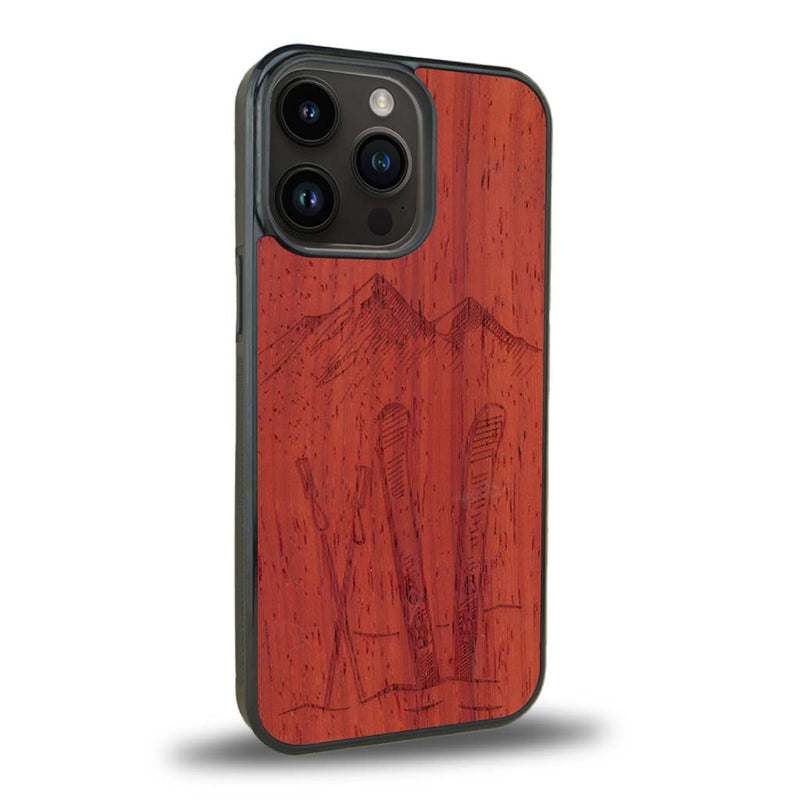 Coque de protection en bois véritable fabriquée en France pour iPhone 15 Pro Max + MagSafe® sur le thème de la montagne, du ski et de la neige avec un motif représentant une paire de ski plantée dans la neige avec en fond des montagnes enneigées