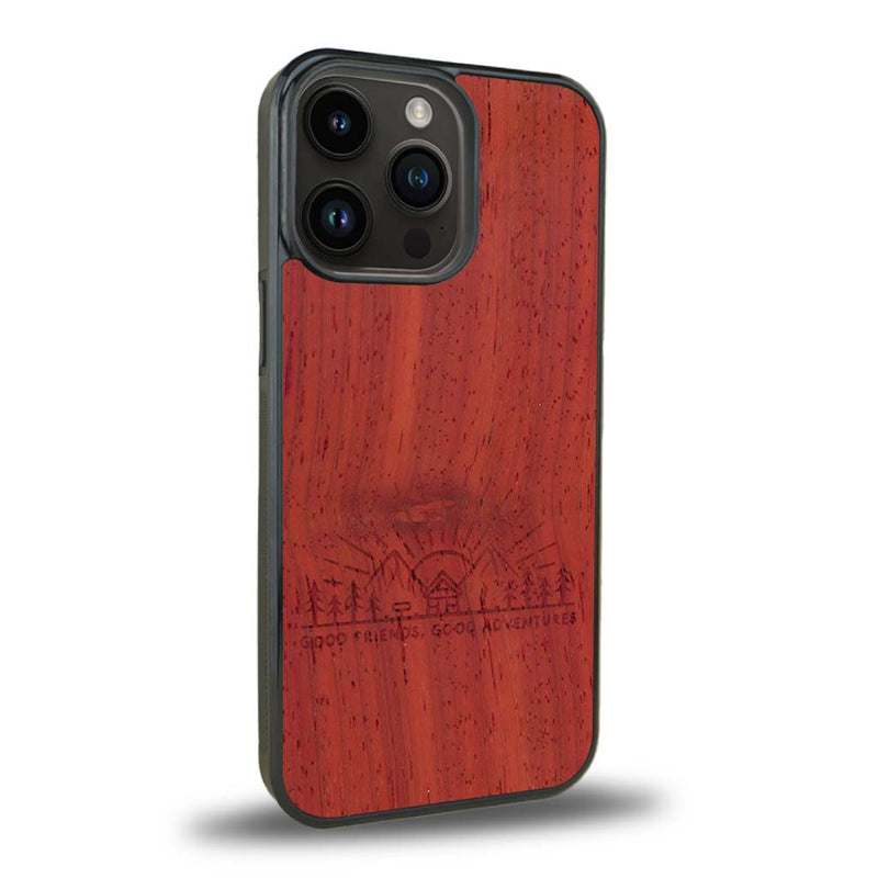 Coque de protection en bois véritable fabriquée en France pour iPhone 15 Pro Max sur le thème chill et nature avec un motif représentant un levé de soleil sur un paysage de montagne avec des sapins et un chalet et la phrase "Good friends, good adventure"