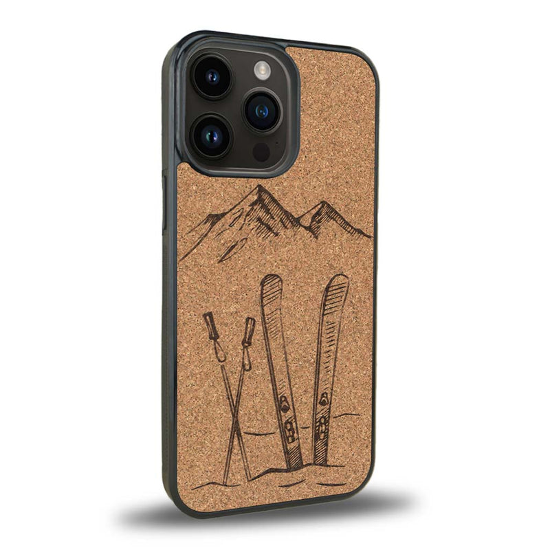 Coque de protection en bois véritable fabriquée en France pour iPhone 15 Pro Max sur le thème de la montagne, du ski et de la neige avec un motif représentant une paire de ski plantée dans la neige avec en fond des montagnes enneigées
