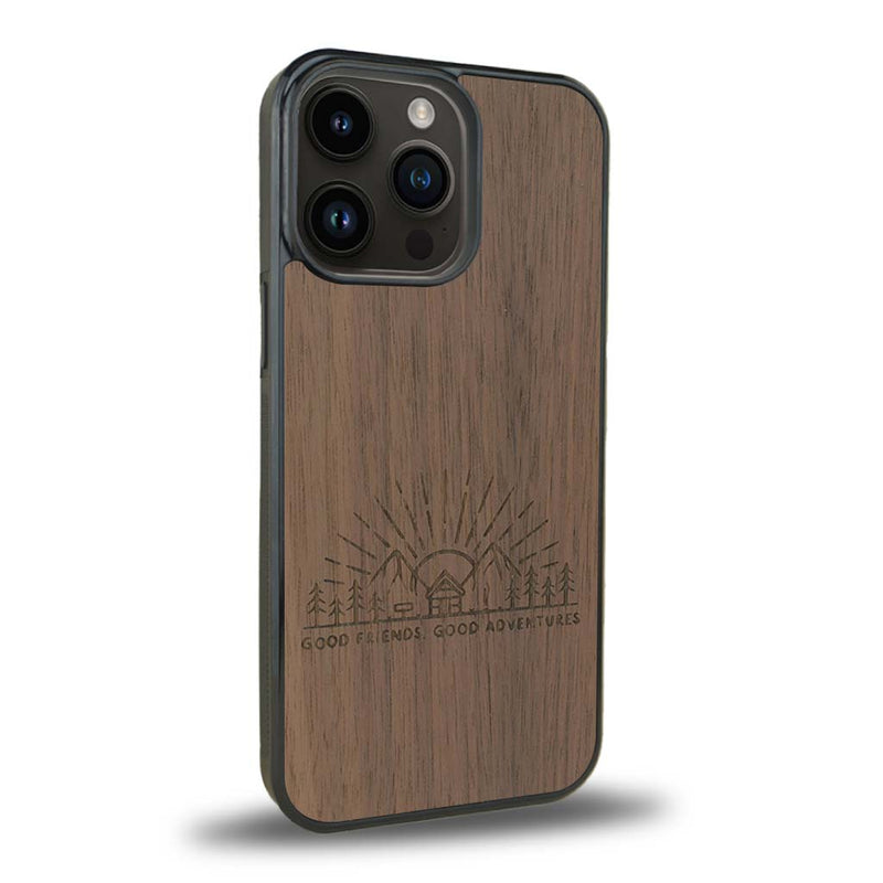 Coque de protection en bois véritable fabriquée en France pour iPhone 15 Pro sur le thème chill et nature avec un motif représentant un levé de soleil sur un paysage de montagne avec des sapins et un chalet et la phrase "Good friends, good adventure"