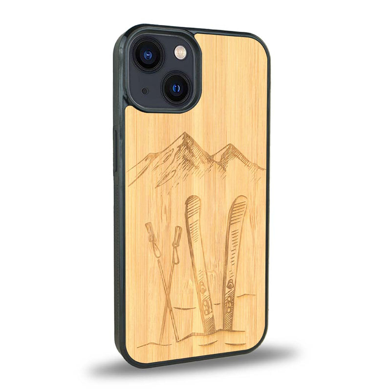 Coque de protection en bois véritable fabriquée en France pour iPhone 15 sur le thème de la montagne, du ski et de la neige avec un motif représentant une paire de ski plantée dans la neige avec en fond des montagnes enneigées