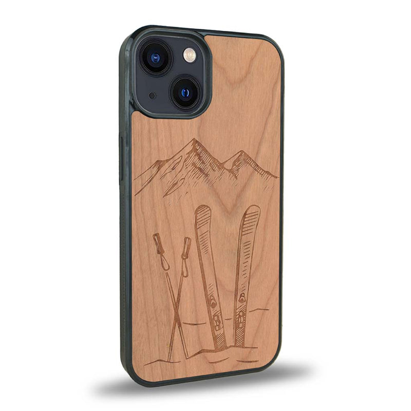 Coque de protection en bois véritable fabriquée en France pour iPhone 15 sur le thème de la montagne, du ski et de la neige avec un motif représentant une paire de ski plantée dans la neige avec en fond des montagnes enneigées