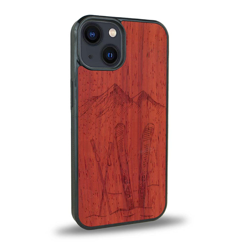 Coque de protection en bois véritable fabriquée en France pour iPhone 15 sur le thème de la montagne, du ski et de la neige avec un motif représentant une paire de ski plantée dans la neige avec en fond des montagnes enneigées