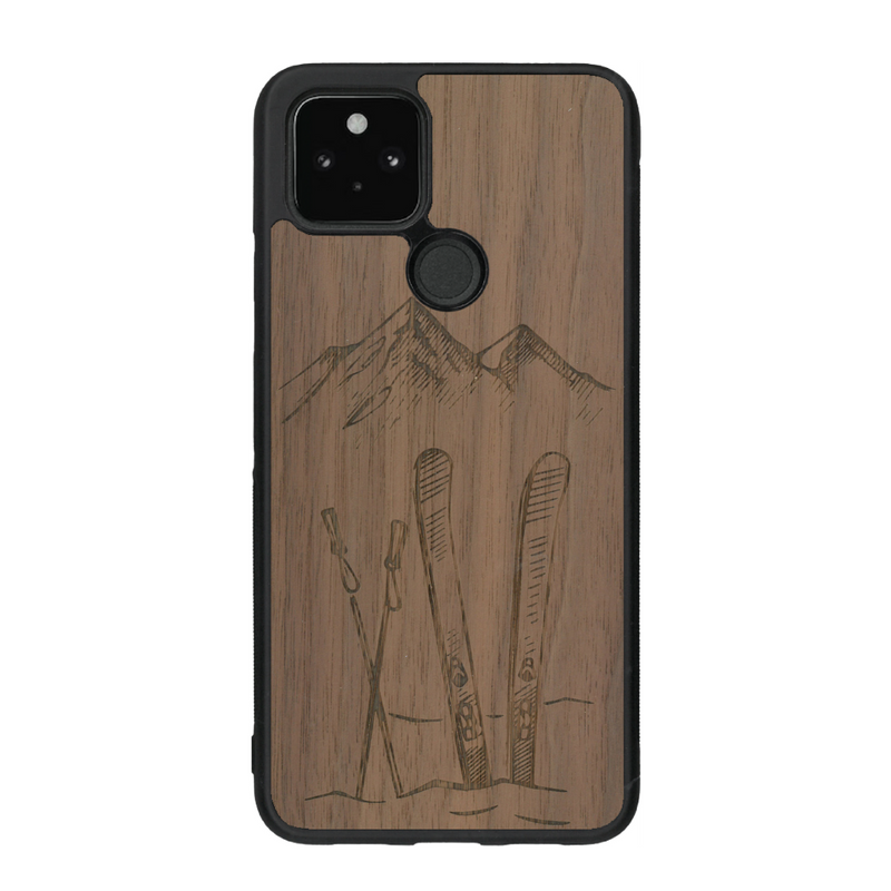 Coque de protection en bois véritable fabriquée en France pour Google Pixel 4a 5g sur le thème de la montagne, du ski et de la neige avec un motif représentant une paire de ski plantée dans la neige avec en fond des montagnes enneigées