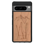 Coque de protection en bois véritable fabriquée en France pour Google Pixel 7 sur le thème de la montagne, du ski et de la neige avec un motif représentant une paire de ski plantée dans la neige avec en fond des montagnes enneigées