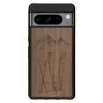 Coque de protection en bois véritable fabriquée en France pour Google Pixel 7 sur le thème de la montagne, du ski et de la neige avec un motif représentant une paire de ski plantée dans la neige avec en fond des montagnes enneigées