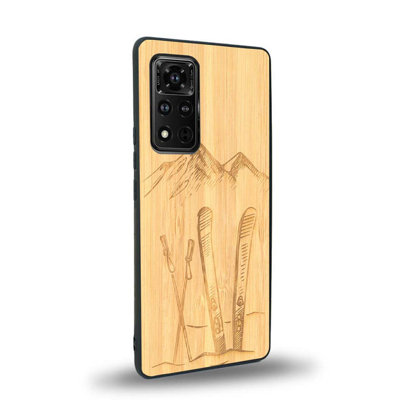 Coque de protection en bois véritable fabriquée en France pour Honor V40 sur le thème de la montagne, du ski et de la neige avec un motif représentant une paire de ski plantée dans la neige avec en fond des montagnes enneigées