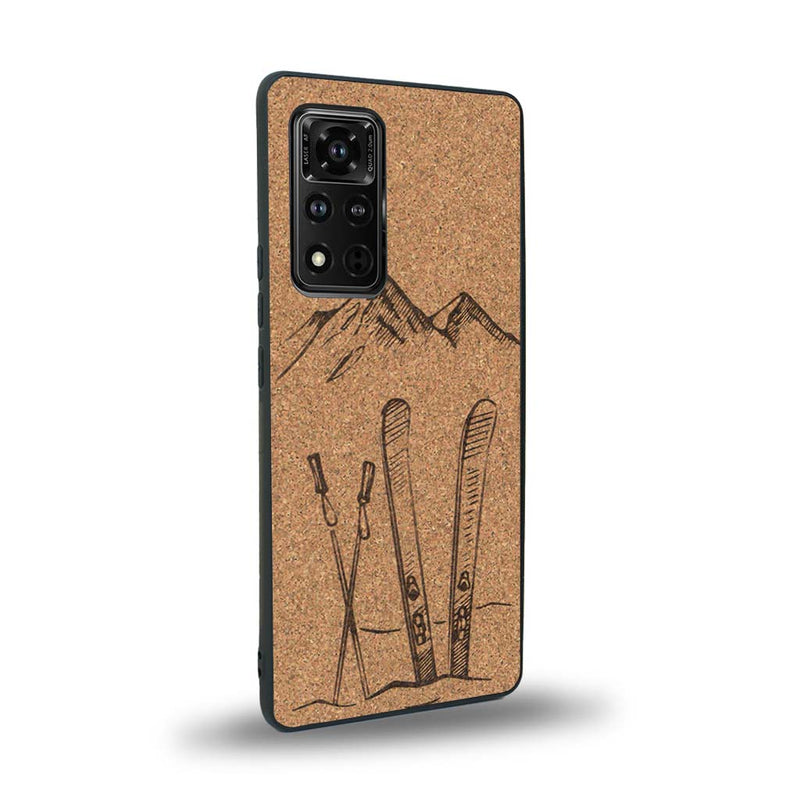 Coque de protection en bois véritable fabriquée en France pour Honor V40 sur le thème de la montagne, du ski et de la neige avec un motif représentant une paire de ski plantée dans la neige avec en fond des montagnes enneigées