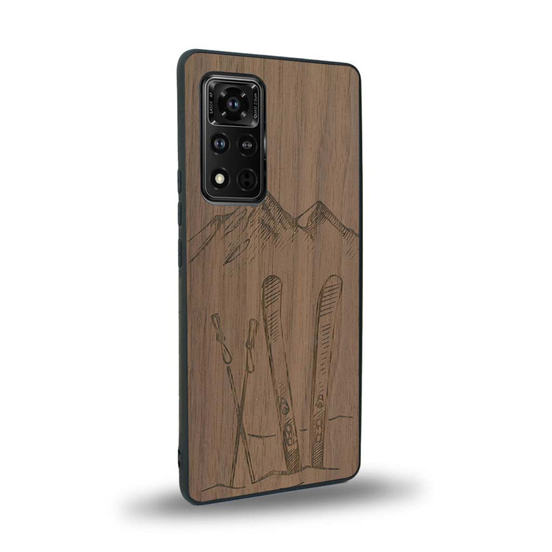 Coque de protection en bois véritable fabriquée en France pour Honor V40 sur le thème de la montagne, du ski et de la neige avec un motif représentant une paire de ski plantée dans la neige avec en fond des montagnes enneigées