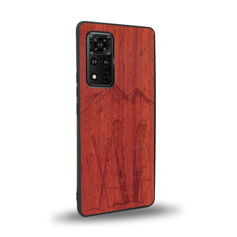 Coque de protection en bois véritable fabriquée en France pour Honor V40 sur le thème de la montagne, du ski et de la neige avec un motif représentant une paire de ski plantée dans la neige avec en fond des montagnes enneigées