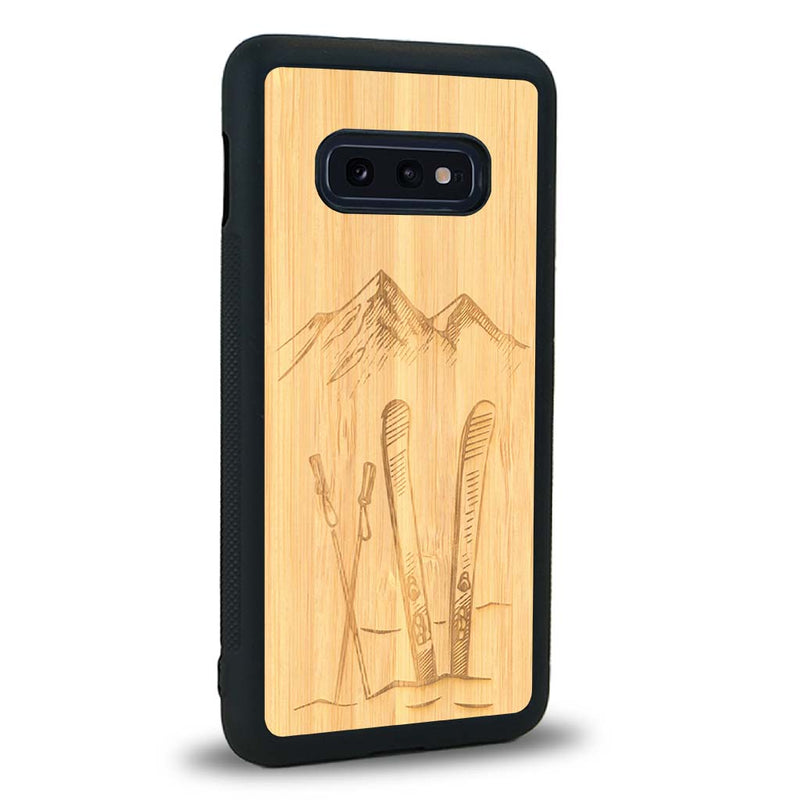 Coque de protection en bois véritable fabriquée en France pour Samsung S10E sur le thème de la montagne, du ski et de la neige avec un motif représentant une paire de ski plantée dans la neige avec en fond des montagnes enneigées