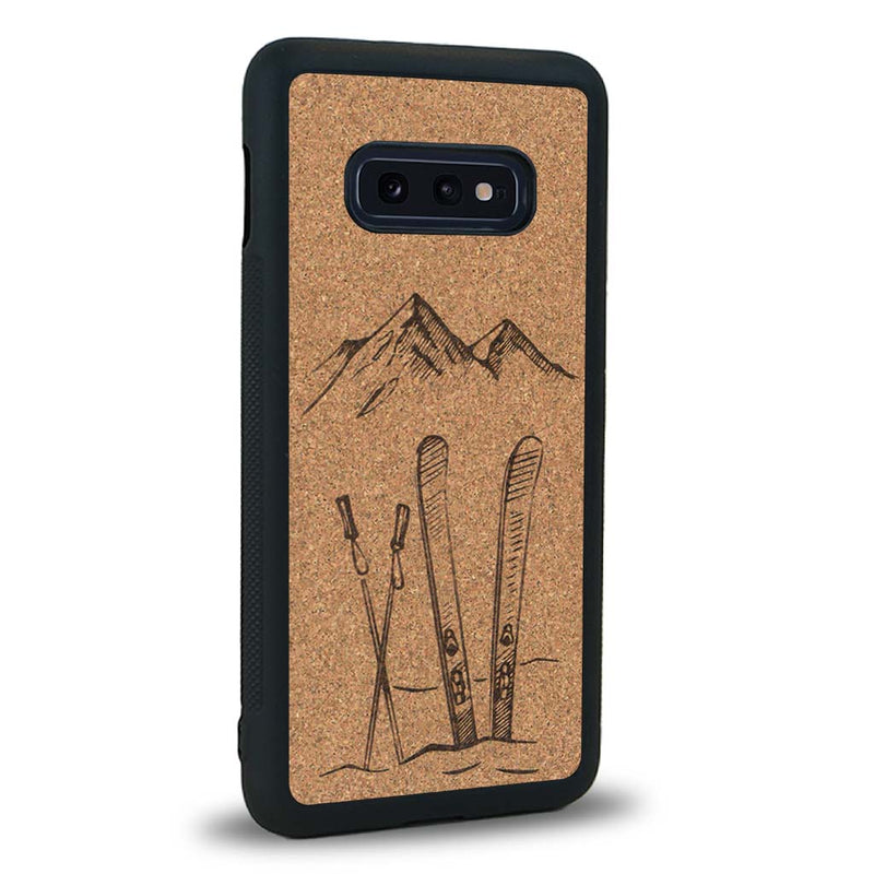 Coque de protection en bois véritable fabriquée en France pour Samsung S10E sur le thème de la montagne, du ski et de la neige avec un motif représentant une paire de ski plantée dans la neige avec en fond des montagnes enneigées
