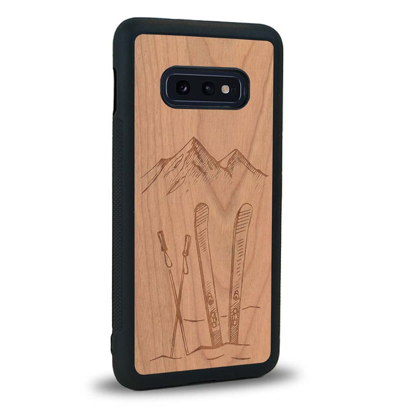 Coque de protection en bois véritable fabriquée en France pour Samsung S10E sur le thème de la montagne, du ski et de la neige avec un motif représentant une paire de ski plantée dans la neige avec en fond des montagnes enneigées