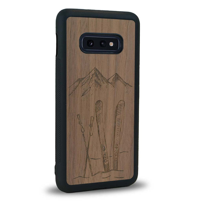 Coque de protection en bois véritable fabriquée en France pour Samsung S10E sur le thème de la montagne, du ski et de la neige avec un motif représentant une paire de ski plantée dans la neige avec en fond des montagnes enneigées