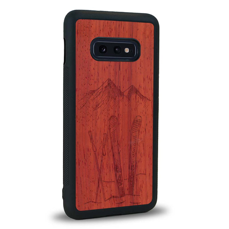 Coque de protection en bois véritable fabriquée en France pour Samsung S10E sur le thème de la montagne, du ski et de la neige avec un motif représentant une paire de ski plantée dans la neige avec en fond des montagnes enneigées