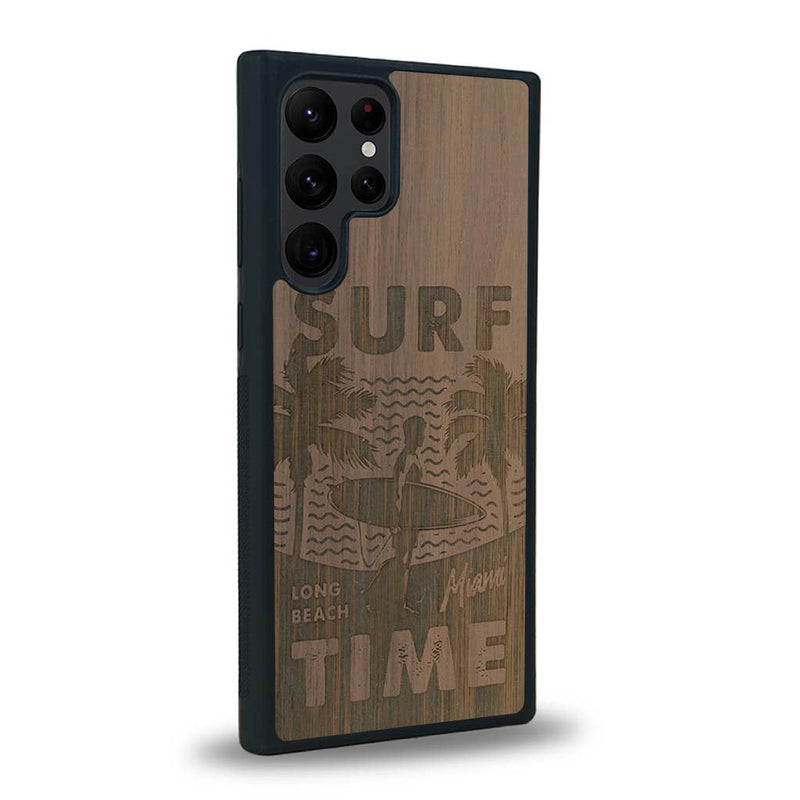 Coque de protection en bois véritable fabriquée en France pour Samsung S23 Ultra sur le thème chill avec un motif représentant une silouhette tenant une planche de surf sur une plage entouré de palmiers et les mots "Surf Time Long Beach Miami"