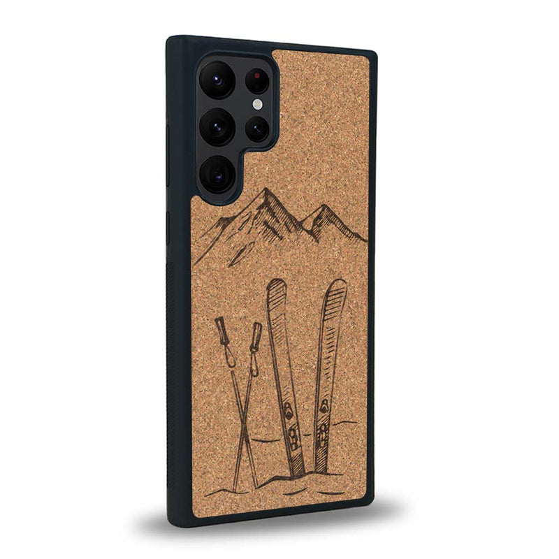 Coque de protection en bois véritable fabriquée en France pour Samsung S23 Ultra sur le thème de la montagne, du ski et de la neige avec un motif représentant une paire de ski plantée dans la neige avec en fond des montagnes enneigées