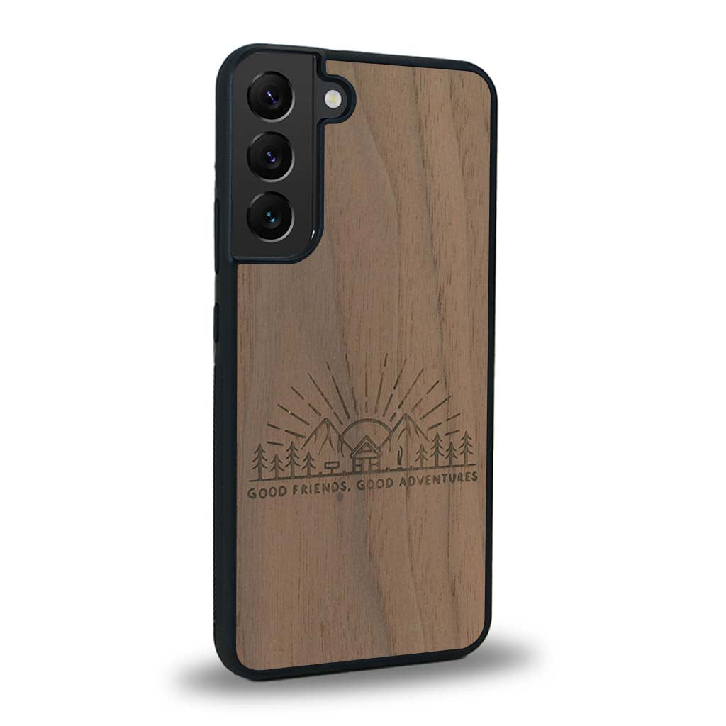 Coque de protection en bois véritable fabriquée en France pour Samsung S23FE sur le thème chill et nature avec un motif représentant un levé de soleil sur un paysage de montagne avec des sapins et un chalet et la phrase "Good friends, good adventure"