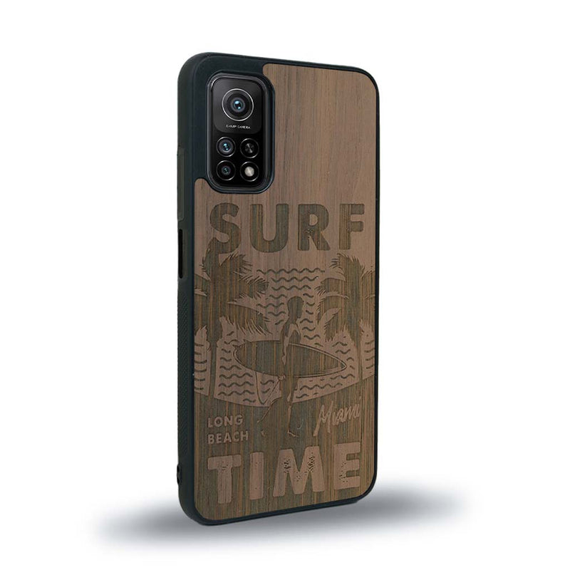 Coque de protection en bois véritable fabriquée en France pour Xiaomi Mi 10 Lite sur le thème chill avec un motif représentant une silouhette tenant une planche de surf sur une plage entouré de palmiers et les mots "Surf Time Long Beach Miami"