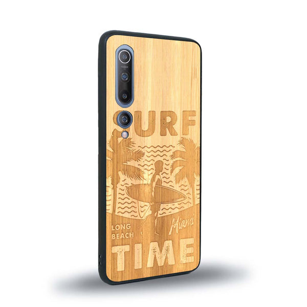 Coque de protection en bois véritable fabriquée en France pour Xiaomi Mi 10 sur le thème chill avec un motif représentant une silouhette tenant une planche de surf sur une plage entouré de palmiers et les mots "Surf Time Long Beach Miami"