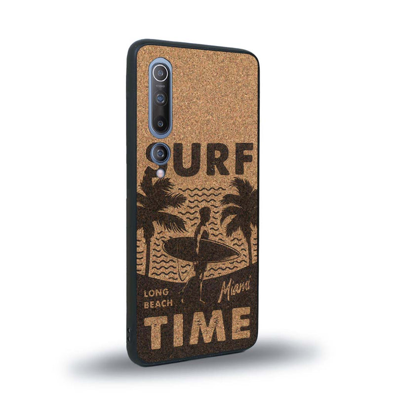 Coque de protection en bois véritable fabriquée en France pour Xiaomi Mi 10 sur le thème chill avec un motif représentant une silouhette tenant une planche de surf sur une plage entouré de palmiers et les mots "Surf Time Long Beach Miami"