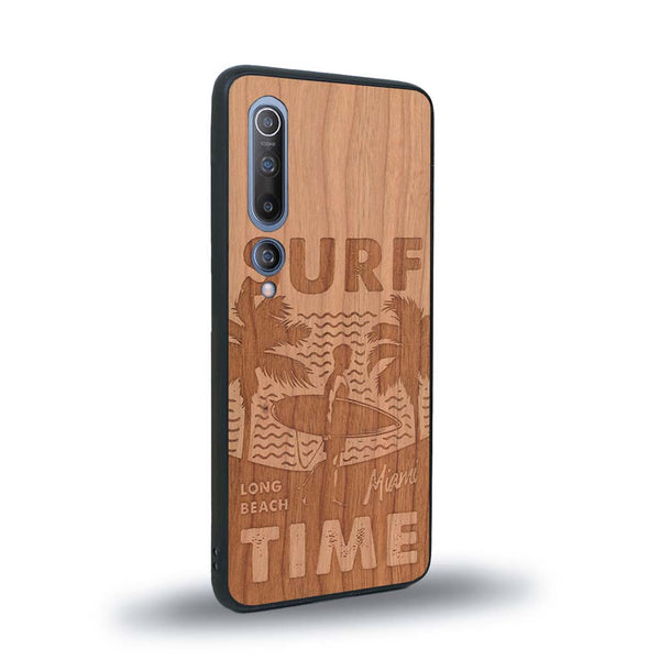 Coque de protection en bois véritable fabriquée en France pour Xiaomi Mi 10 sur le thème chill avec un motif représentant une silouhette tenant une planche de surf sur une plage entouré de palmiers et les mots "Surf Time Long Beach Miami"