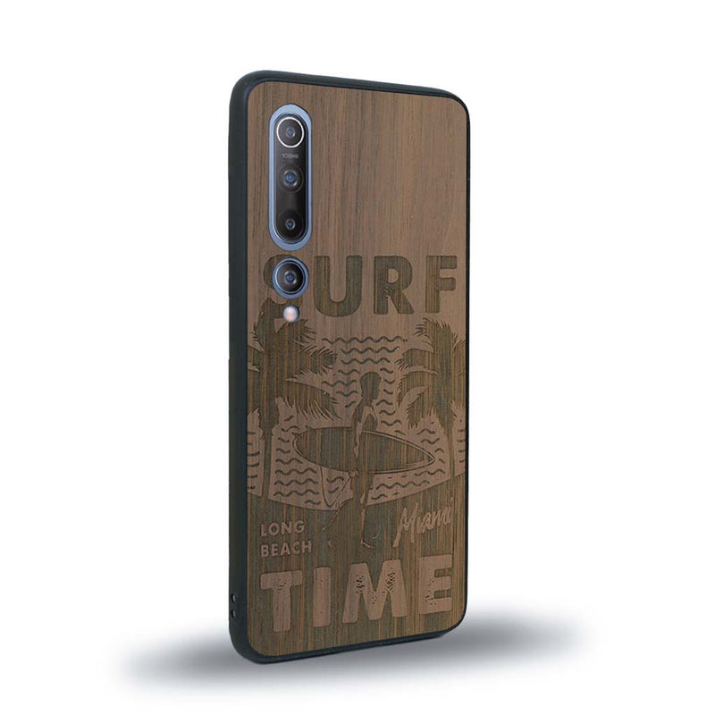 Coque de protection en bois véritable fabriquée en France pour Xiaomi Mi 10 sur le thème chill avec un motif représentant une silouhette tenant une planche de surf sur une plage entouré de palmiers et les mots "Surf Time Long Beach Miami"