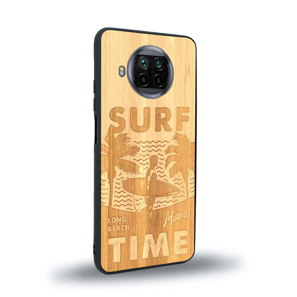 Coque de protection en bois véritable fabriquée en France pour Xiaomi Mi 10T Lite sur le thème chill avec un motif représentant une silouhette tenant une planche de surf sur une plage entouré de palmiers et les mots "Surf Time Long Beach Miami"