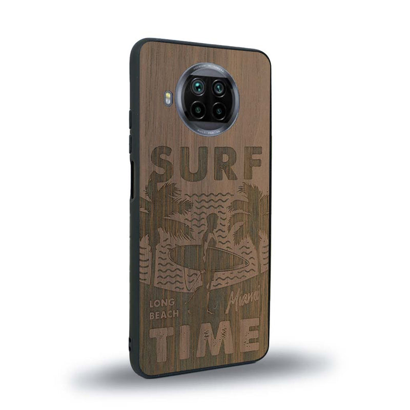 Coque de protection en bois véritable fabriquée en France pour Xiaomi Mi 10T Lite sur le thème chill avec un motif représentant une silouhette tenant une planche de surf sur une plage entouré de palmiers et les mots "Surf Time Long Beach Miami"